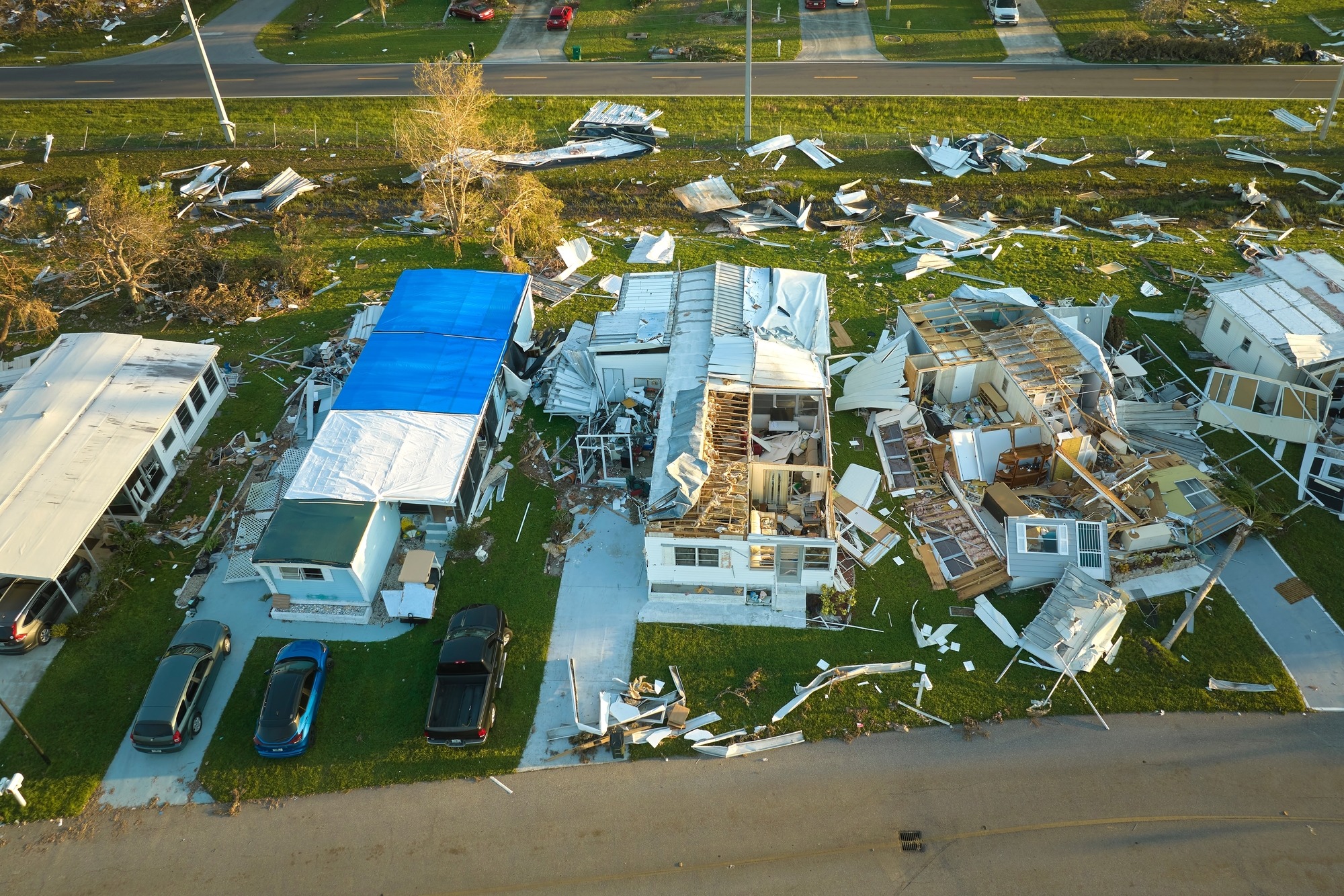 Damaged homes after a severe storm, showcasing extensive destruction with debris scattered across the lawn and roofs stripped away.