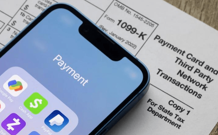 Smartphone displaying a "Payment" screen with icons for various payment apps, positioned next to a 1099-K tax form. Relevant for financial transaction topics.