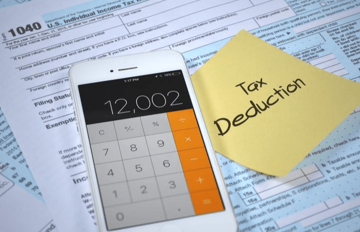 Calculator displaying "12,002" next to tax forms and a sticky note labeled "Tax Deduction," illustrating tax preparation and planning.