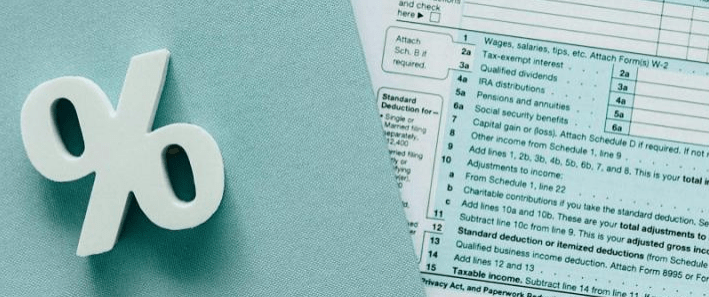 White percentage symbol on a light blue surface next to a partially visible tax form, highlighting financial calculations relevant to tax returns.