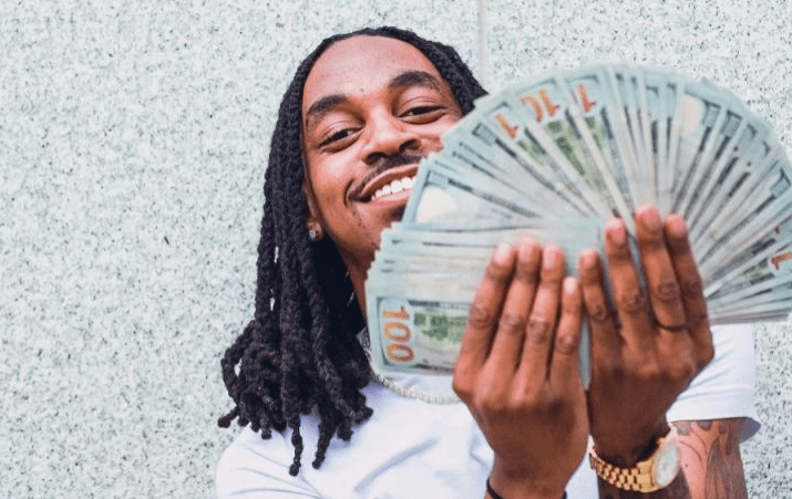Young man smiling and holding a large fan of cash, showcasing enthusiasm and success against a neutral background.