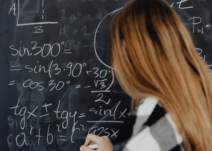 Student solving mathematical equations on a chalkboard, illustrating trigonometric functions and algebraic expressions.