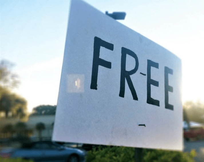 Sign reading "FREE" in bold letters, promoting an offer. A blurred background hints at a parking area or street setting, emphasizing availability.