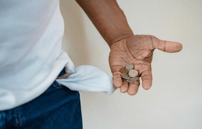 A person holds coins in their outstretched hand, with an empty pocket visible, symbolizing financial struggles.