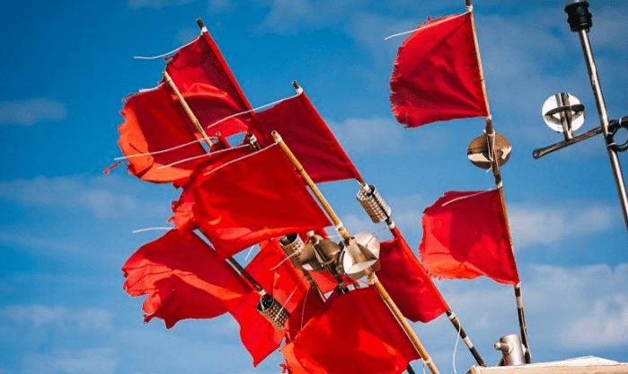 Bright red flags flutter against a blue sky, indicating caution or warning. The scene is likely maritime, suggesting safety measures in use.