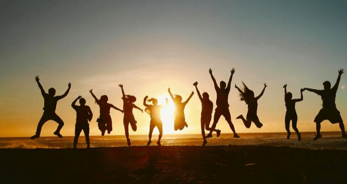 Silhouetted group of people joyfully jumping against a sunset backdrop at the beach, symbolizing celebration and togetherness.