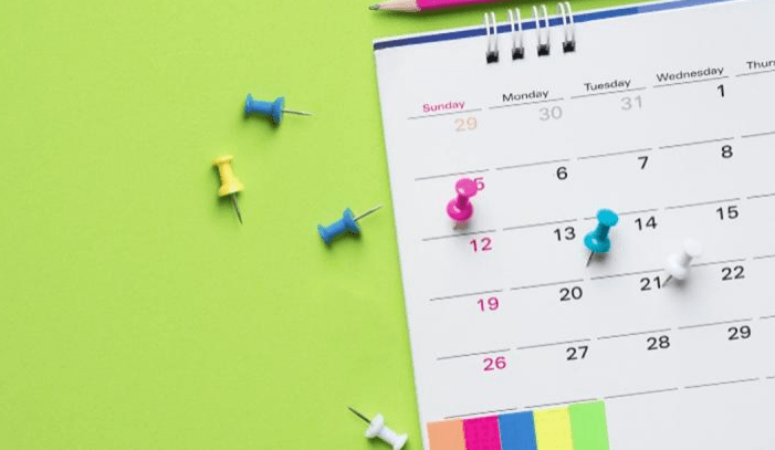 Colorful push pins and a pencil are arranged around a calendar on a bright green background, emphasizing organization and planning.