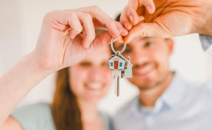 New homeowners proudly display a house-shaped keychain with keys, symbolizing their recent property purchase and new beginnings.