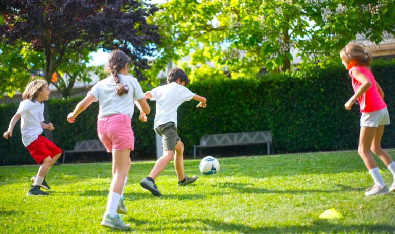 Four children play soccer on a sunny green lawn, showcasing teamwork and joy in outdoor activities. The vibrant scene emphasizes active play.