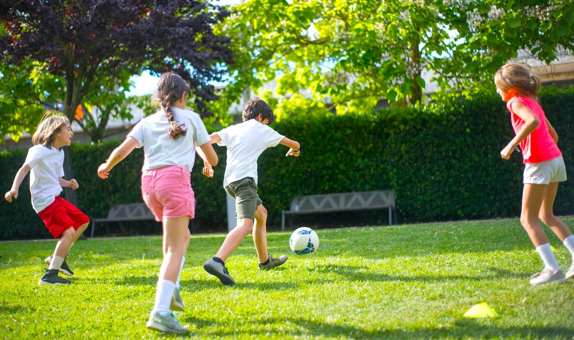 Four children play soccer on a sunny green lawn, showcasing teamwork and joy in outdoor activities. The vibrant scene emphasizes active play.