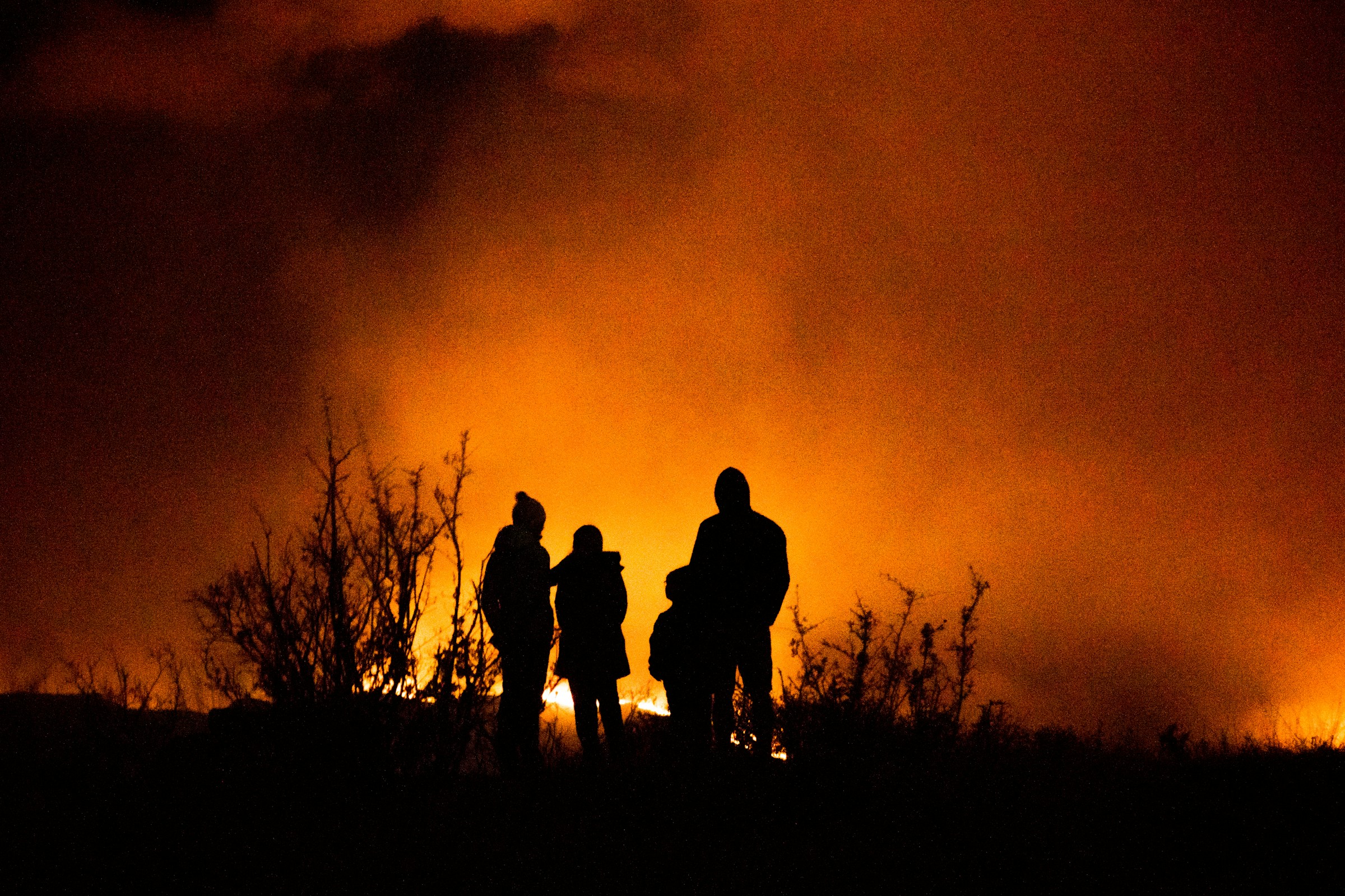Silhouettes of four people stand against a fiery orange background, likely from a wildfire, highlighting the urgency of environmental issues.