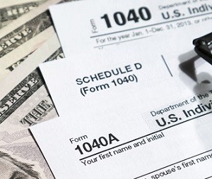 U.S. tax forms 1040 and Schedule D displayed atop dollar bills, highlighting financial documentation and tax preparation relevance.