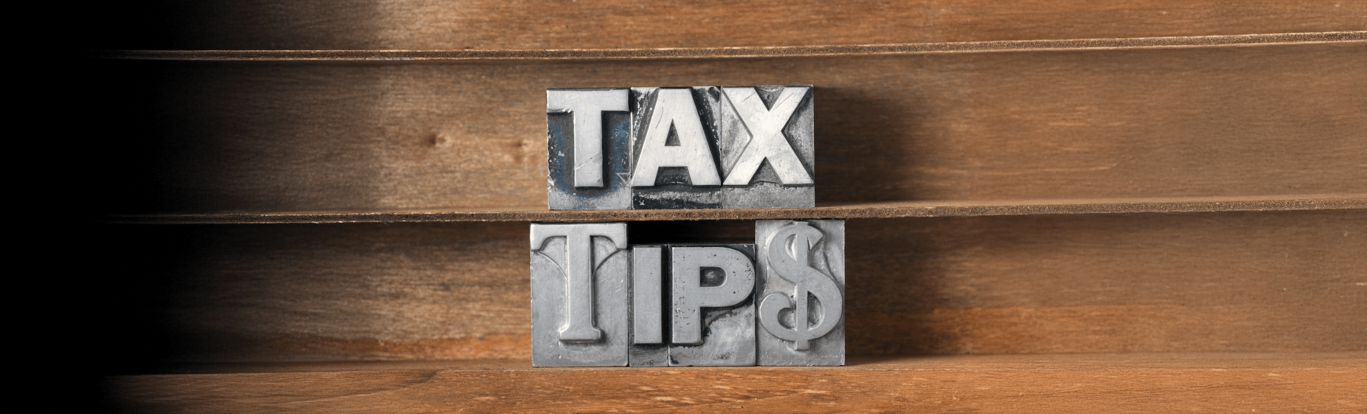 "Bold metal letterpress blocks spelling 'TAX TIPS' on wooden shelves, symbolizing financial advice and tax preparation guidance."