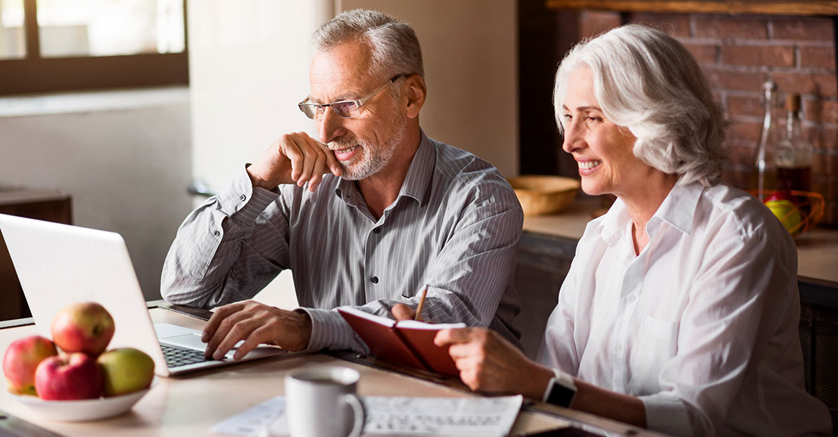 older couple at kitchen table reviewing finances on laptop