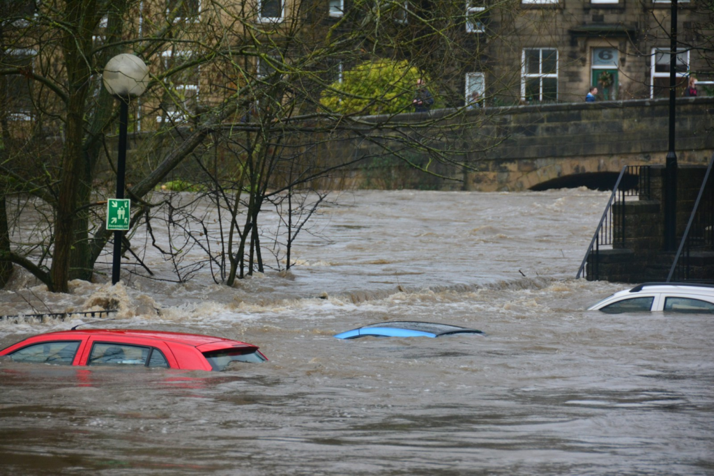 Three cars partially submerged in a flooded river near a stone bridge